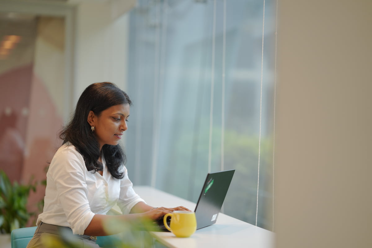 A woman sitting at a counter by a window working on her laptop