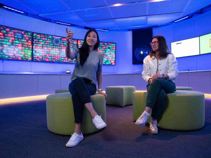 two women sitting on poufs in a room with screens and a wall with screens