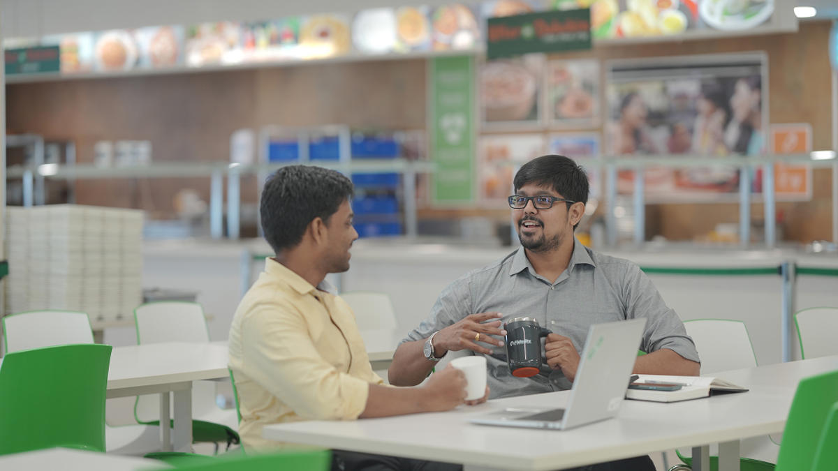 two men sitting at a table with coffee cups and laptop