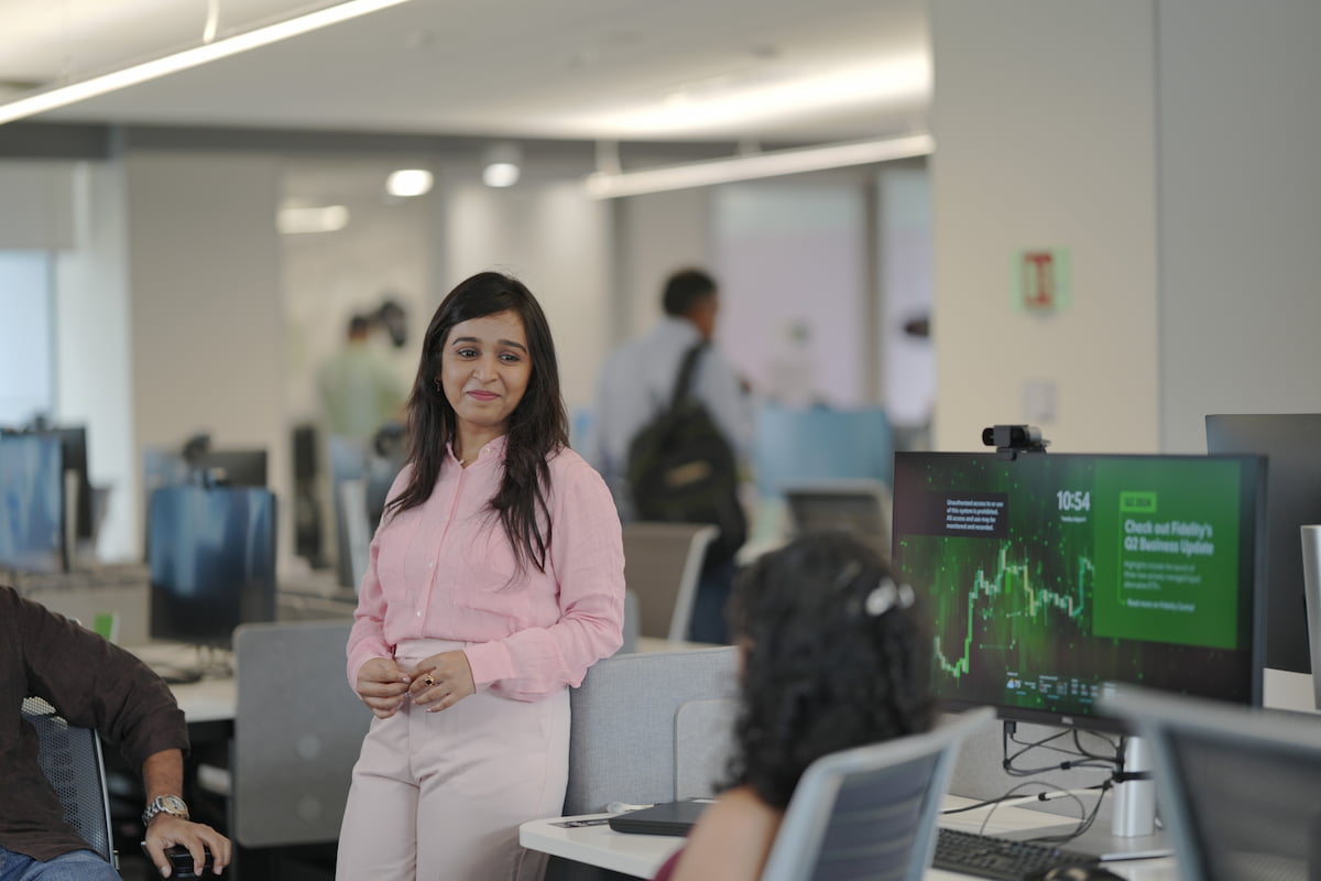 A woman standing next to another, seated woman as they are talking in an office