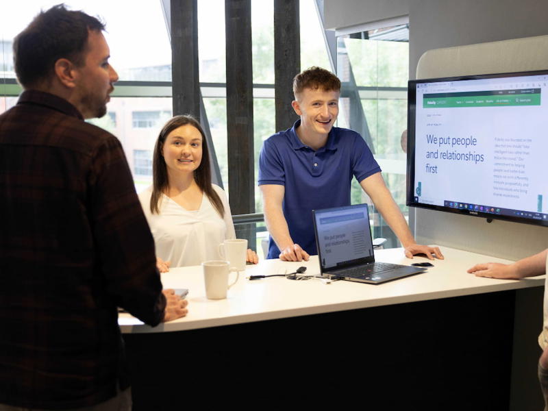 a group of people standing around a table with a laptop