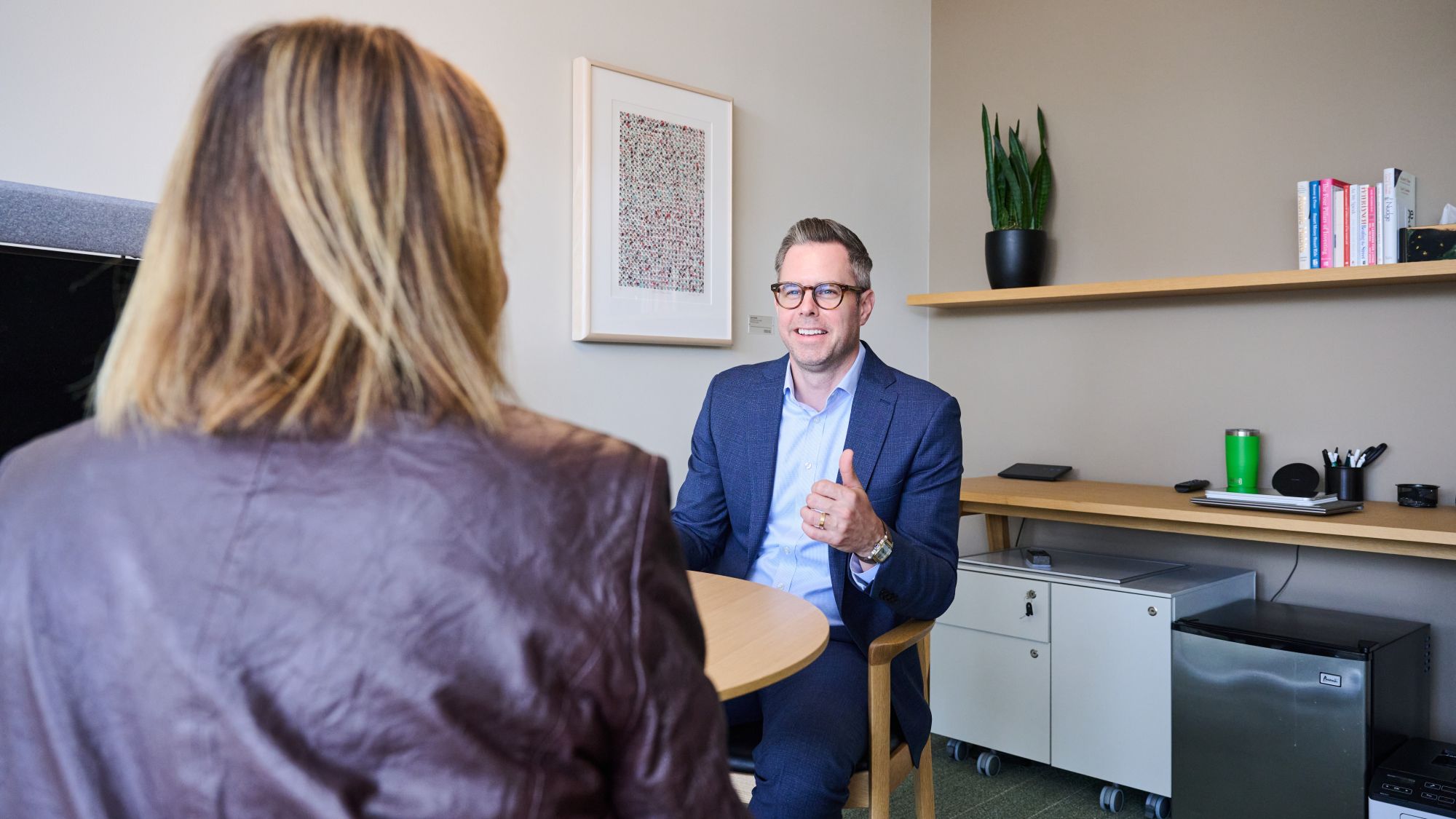 a person in a suit sitting at a table with a person in a purple jacket