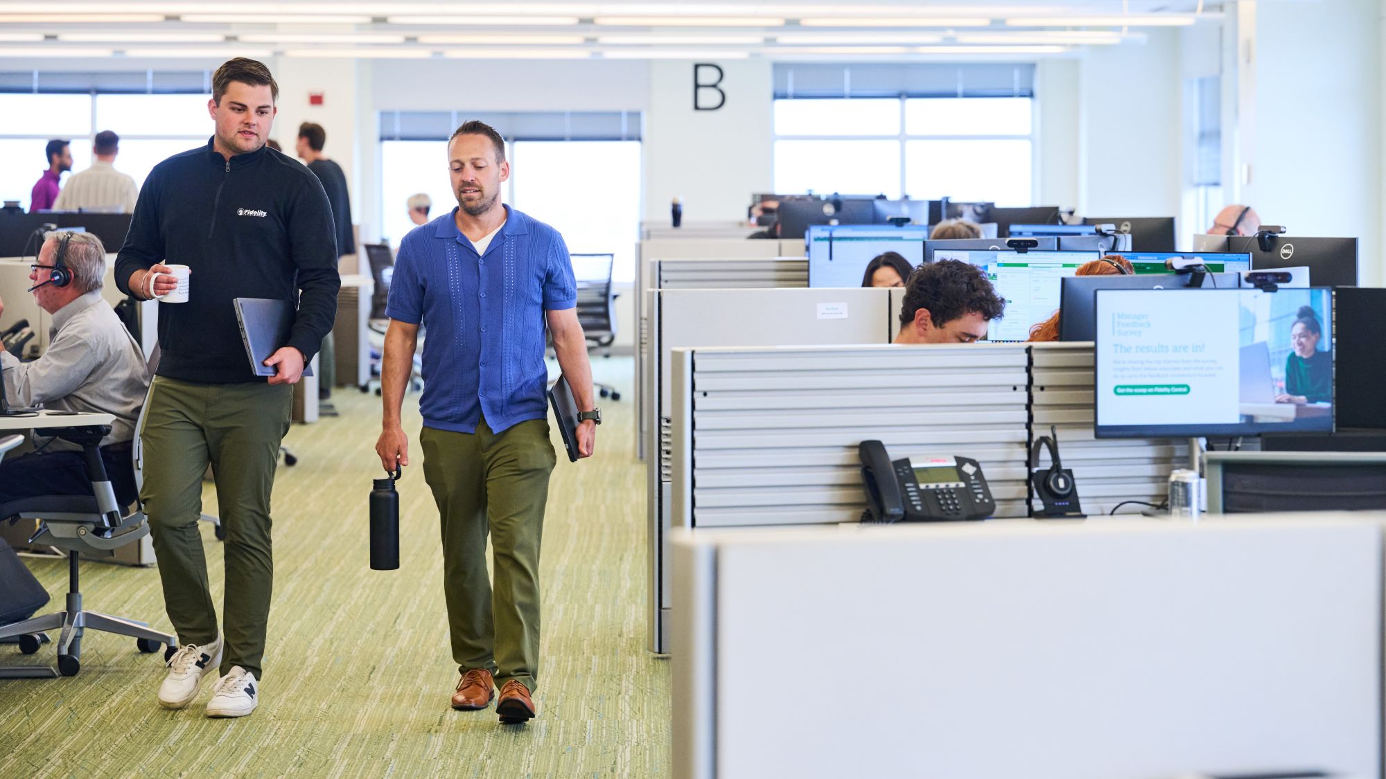 a person walking in an office with a person holding a black bottle