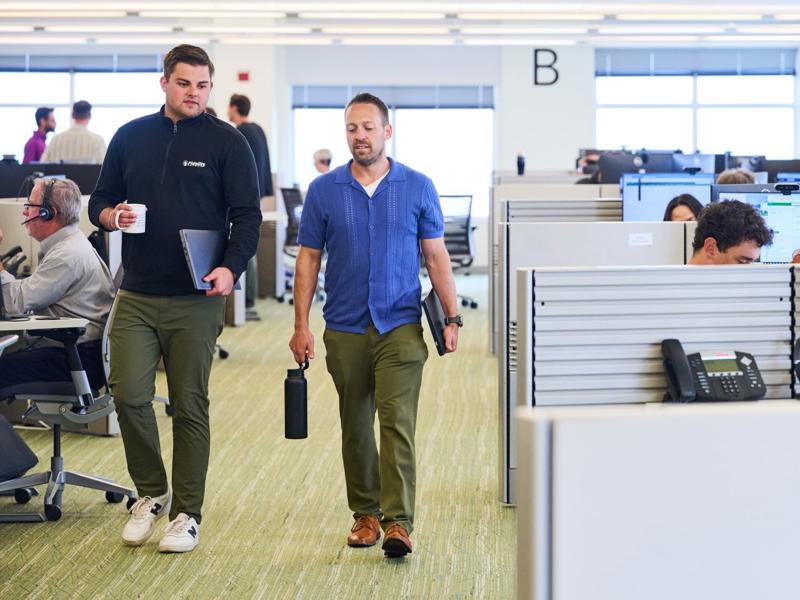 a person walking in an office with a person holding a black bottle