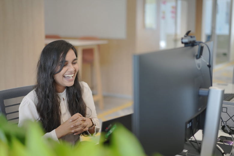 A woman with a wide smile sitting in front of a computer monitor