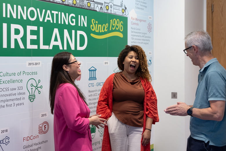 Three Fidelity associates laughing as they talk in front of a sign that says "Innovating in Ireland since 1996"