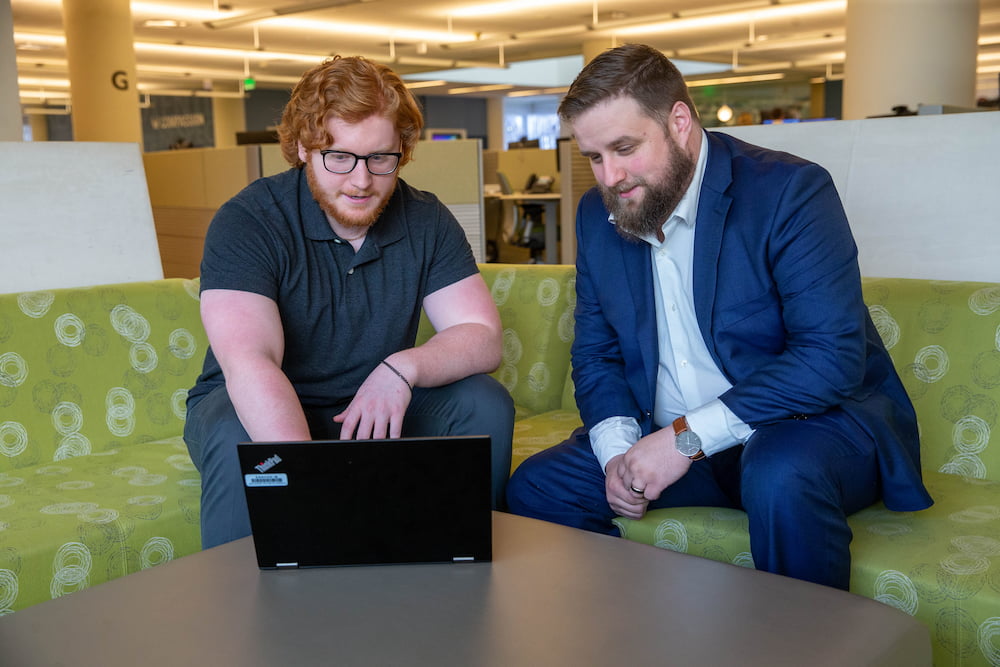 One man explaining something on his laptop to another man sitting next to him
