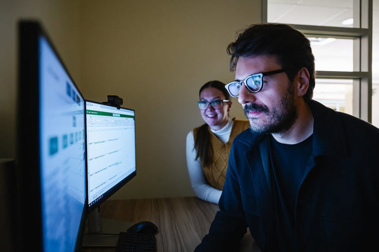 A man using a computer in the foreground with a woman looking on behind him