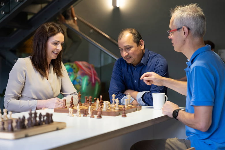 Two people playing chess in a break room with a third person watching