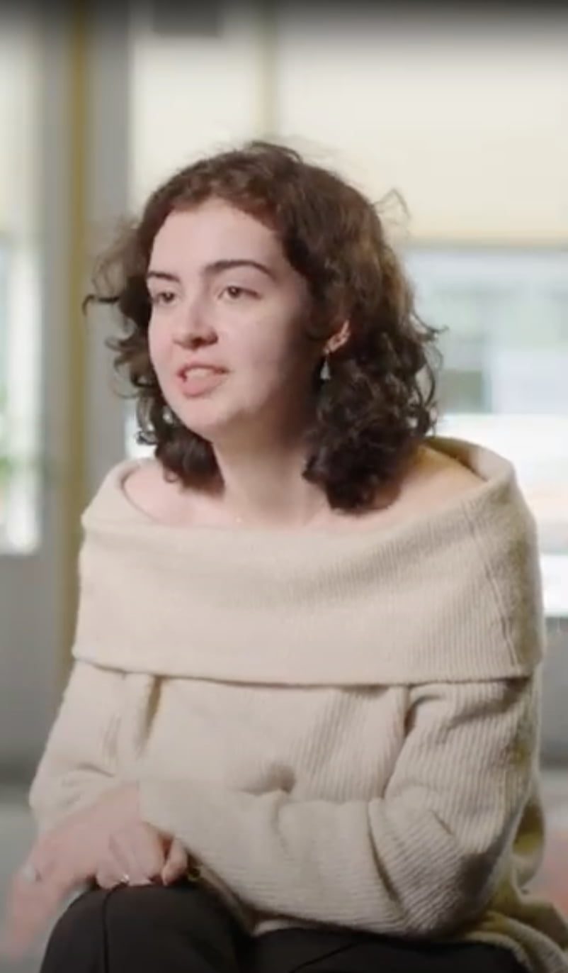 a person with curly hair wearing a beige sweater
