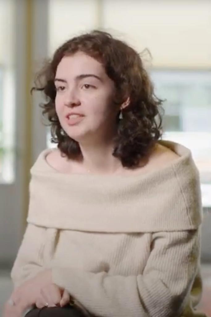 a person with curly hair wearing a beige sweater