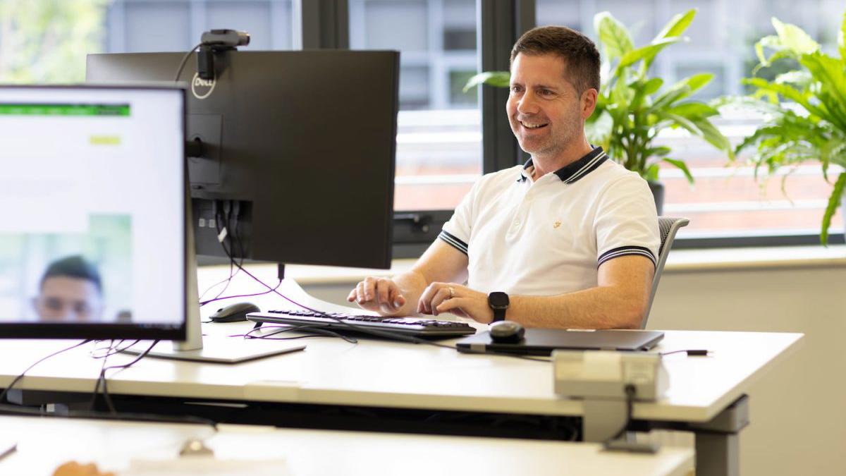 Person Smiling Computer Desk Sunny Office 1200X800