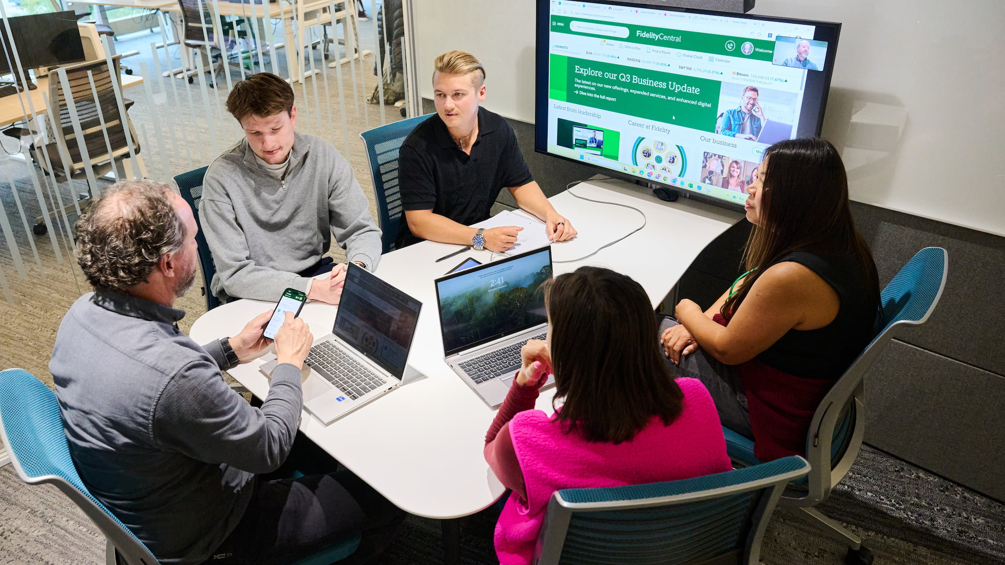 a group of people sitting around a table with laptops