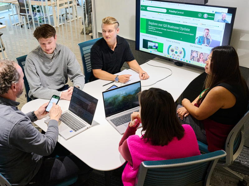 a group of people sitting around a table with laptops