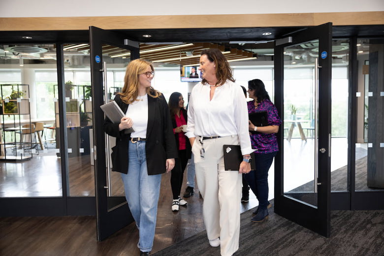 Two women walking together through an office door