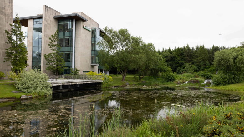 An external photo of Fidelity's office in Ireland, with a pond and trees surrounding it