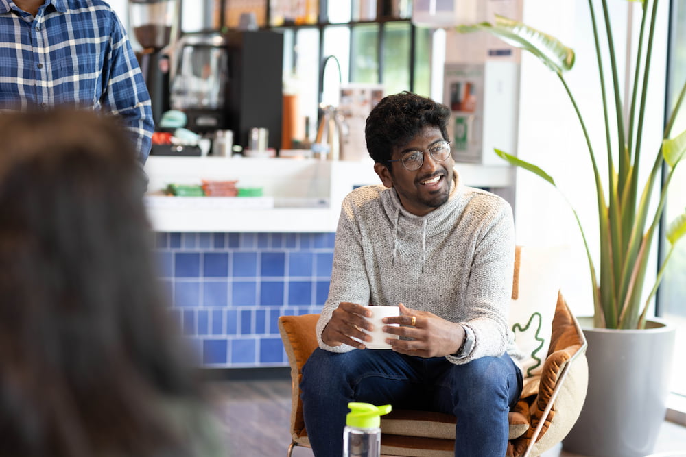 A man smiling while sitting in a chair and holding a coffee cup