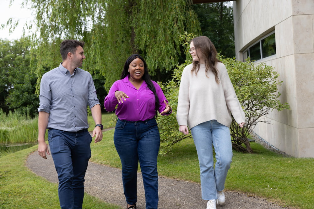 Three Fidelity employees chatting while they walk on a path around a Fidelity office