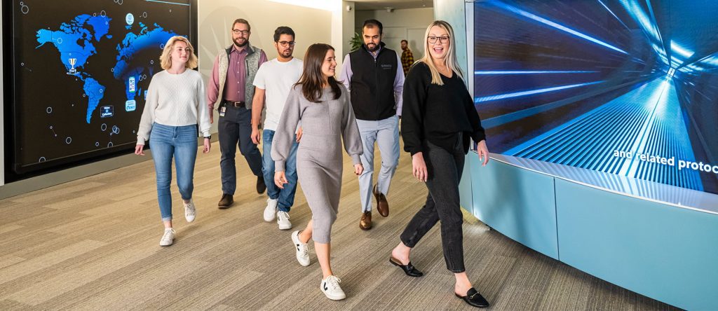 Several Fidelity associates walking along a curved hallway with a large map of the world and high tech graphics behind them